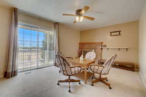 Carpeted dining space featuring a brick fireplace and ceiling fan