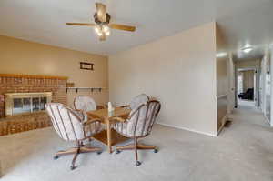 Dining space with ceiling fan, carpet flooring, and a brick fireplace