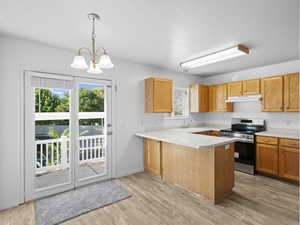 Kitchen featuring light wood-type flooring, ventilation hood, range, decorative light fixtures, and kitchen peninsula