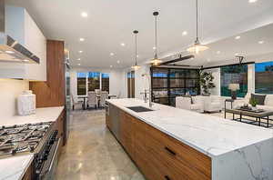 EXAMPLE Of Kitchen featuring a center island with sink, hanging light fixtures, wall chimney exhaust hood, sink, and appliances with stainless steel finishes