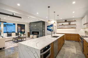 EXAMPLE Of Kitchen featuring light stone counters, a fireplace, appliances with stainless steel finishes, sink, and a large island