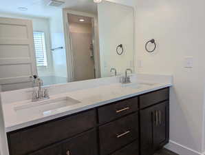 Bathroom with dual sinks, vanity with extensive cabinet space, and an enclosed shower