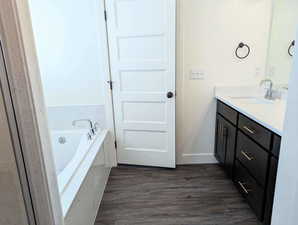 Bathroom with tiled tub, hardwood / wood-style floors, and vanity