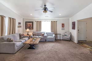 Living room featuring ceiling fan, carpet flooring, and lofted ceiling