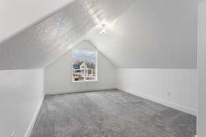 Additional living space featuring vaulted ceiling, a textured ceiling, and carpet flooring