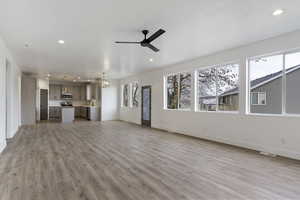 Unfurnished living room featuring a wealth of natural light, sink, light hardwood / wood-style floors, and ceiling fan with notable chandelier