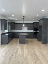 Kitchen with a kitchen island, light hardwood / wood-style flooring, double oven, pendant lighting, and sink