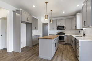 Kitchen with butcher block counters, stainless steel appliances, hardwood / wood-style floors, pendant lighting, and sink