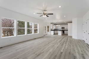 Unfurnished living room with ceiling fan with notable chandelier and light hardwood / wood-style flooring