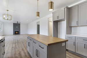 Kitchen with decorative light fixtures, a kitchen island, light wood-type flooring, wooden counters, and a tile fireplace