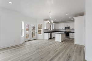 Kitchen with light hardwood / wood-style floors, hanging light fixtures, white cabinetry, appliances with stainless steel finishes, and sink