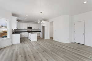 Kitchen with white cabinetry, a kitchen island, light wood-type flooring, decorative light fixtures, and sink