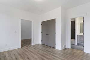 Unfurnished bedroom with a closet, ensuite bathroom, and light wood-type flooring