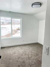 Unfurnished room with vaulted ceiling, carpet, and a textured ceiling