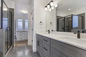 Bathroom featuring tile flooring, vanity with extensive cabinet space, an enclosed shower, and double sink