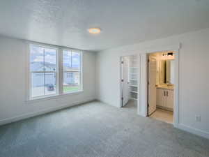 Unfurnished bedroom featuring light carpet, connected bathroom, sink, and a textured ceiling