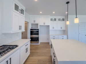 Kitchen with white cabinets, backsplash, light hardwood / wood-style floors, and appliances with stainless steel finishes