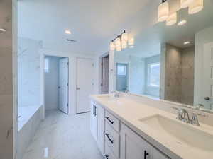 Bathroom featuring a relaxing tiled tub, dual vanity, and tile patterned floors