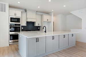 Kitchen featuring tasteful backsplash, light wood-type flooring, black microwave, sink, and a kitchen island with sink