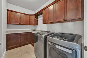 Clothes washing area with cabinets, washer and clothes dryer, and light tile floors