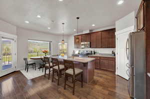 Kitchen featuring dark hardwood / wood-style flooring, stainless steel appliances, a kitchen island with sink, pendant lighting, and sink