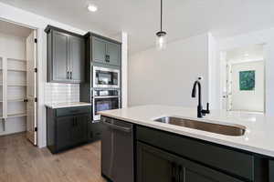 Kitchen featuring appliances with stainless steel finishes, light hardwood / wood-style flooring, sink, pendant lighting, and backsplash