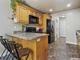 Kitchen featuring kitchen peninsula, black appliances, light stone counters, light tile floors, and a breakfast bar area