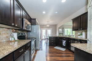 Kitchen featuring stainless steel appliances, stone backsplash, dark wood-type flooring, and large countertops