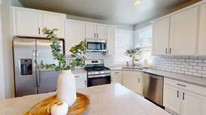 Kitchen featuring appliances with stainless steel finishes, white cabinetry, sink, and tasteful backsplash