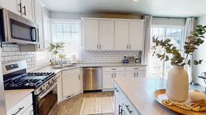 Kitchen featuring appliances with stainless steel finishes, light laminate floors, white cabinets, and tasteful backsplash