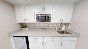 Basement kitchenette featuring backsplash, white cabinets, sink, microwave, refrigerator, and light laminate flooring