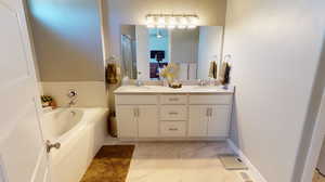 Ensuite bathroom with vinyl tile flooring, double sink vanity, and a bath to relax in