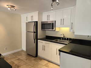 Kitchen featuring white cabinetry, sink, rail lighting, and stainless steel appliances