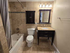 Full bathroom featuring shower / bath combo with shower curtain, tile flooring, tile walls, and vanity