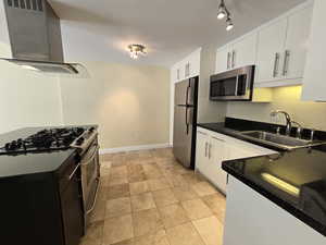 Kitchen with wall chimney range hood, stainless steel appliances, rail lighting, white cabinets, and light tile floors