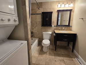 Full bathroom featuring shower / tub combination, tile floors, stacked washer and dryer, tile walls, and vanity