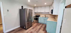 Kitchen featuring blue cabinets, sink, light hardwood / wood-style floors, and appliances with stainless steel finishes