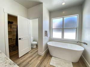 Master bathroom with plenty of natural light, a washtub, toilet, and hardwood / wood-style floors