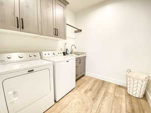 Washroom with separate washer and dryer, sink, light hardwood / wood-style flooring, and cabinets