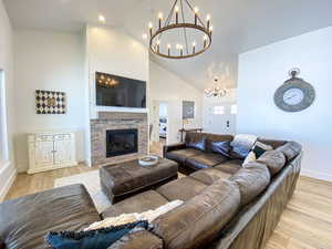 Living room with high vaulted ceiling, a fireplace, an inviting chandelier, and light hardwood / wood-style flooring