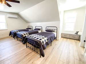 Bedroom featuring ceiling fan, light wood-type flooring, vaulted ceiling, and an AC wall unit