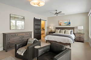 Carpeted bedroom featuring a barn door, ensuite bathroom, and ceiling fan