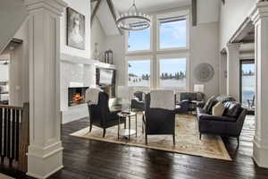 Living room featuring a fireplace, dark hardwood / wood-style floors, a chandelier, ornate columns, and high vaulted ceiling