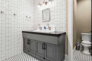 Bathroom featuring tile flooring, tile walls, toilet, and vanity