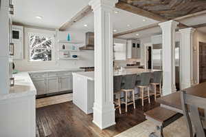 Kitchen with dark wood-type flooring, ornate columns, wall chimney exhaust hood, and tasteful backsplash