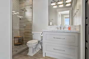 Bathroom with a tile shower, large vanity, a notable chandelier, and toilet