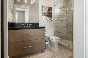 Bathroom featuring a tile shower, vanity with extensive cabinet space, tile flooring, and toilet