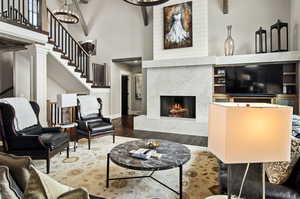 Living room with dark wood-type flooring, a fireplace, beamed ceiling, a high ceiling, and ornate columns