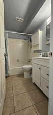 Full bathroom featuring toilet, tile floors, shower / bath combo with shower curtain, vanity, and a textured ceiling