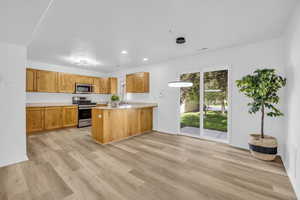 Kitchen featuring light hardwood / wood-style floors, kitchen peninsula, appliances with stainless steel finishes, sink, and pendant lighting